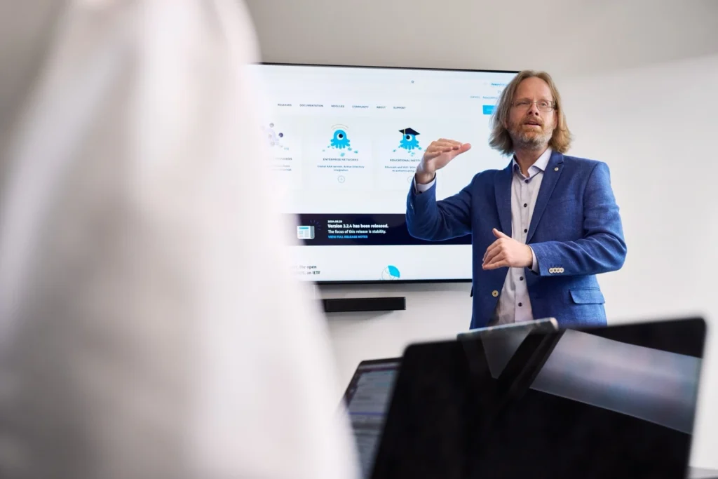 A man in a suit presenting to a group of people in a conference room.